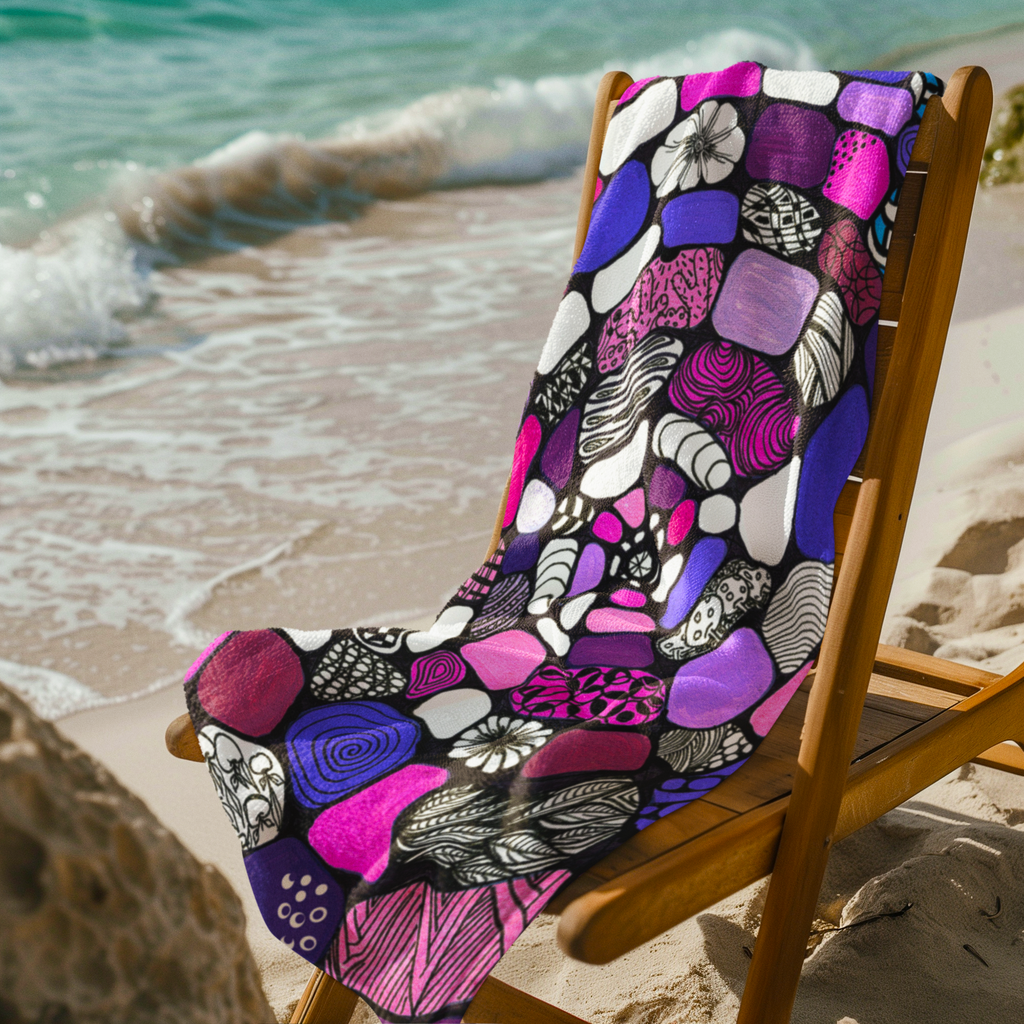 Vibrant abstract doodle art blanket in pink, purple, and black draped on beach chair by ocean waves